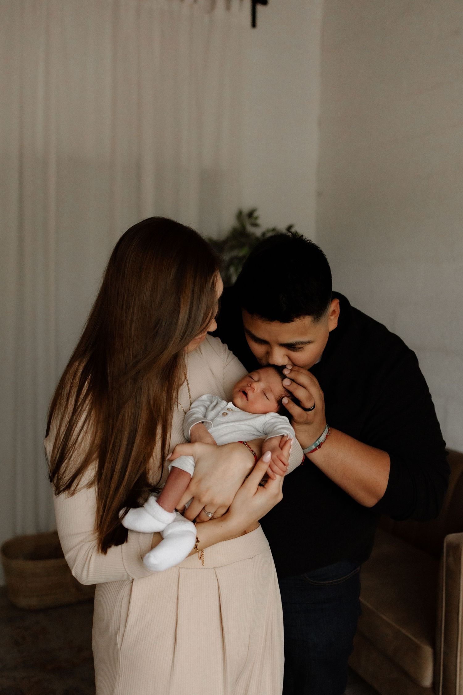 Intimate family moment with newborn baby in a minimalist white room setting.