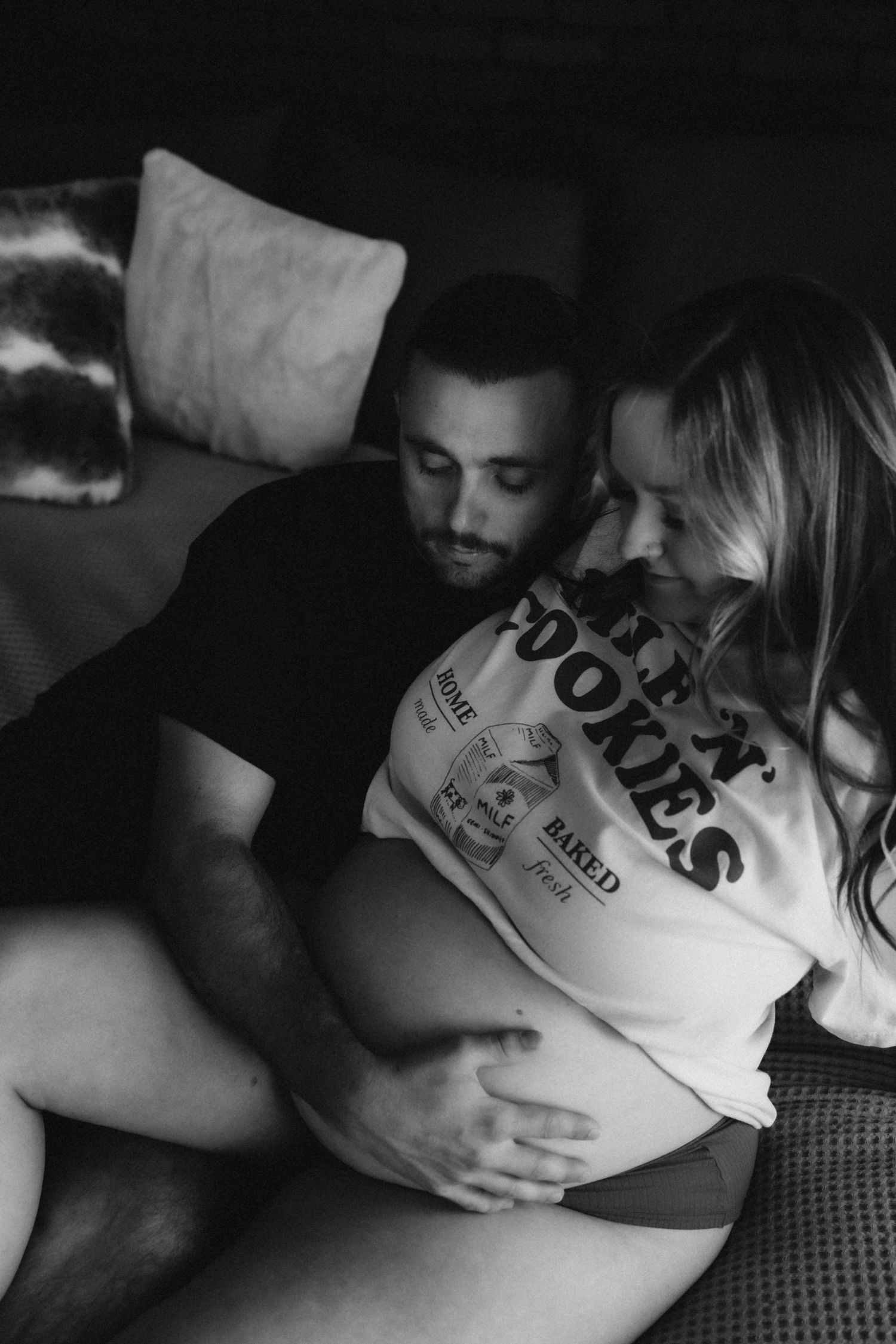 An intimate black and white maternity photo of a couple sharing a moment on a couch.