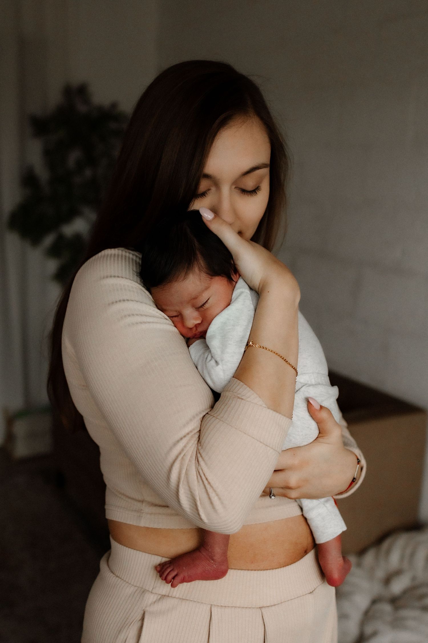 Tender moment with sleeping baby in white clothing against neutral backdrop.