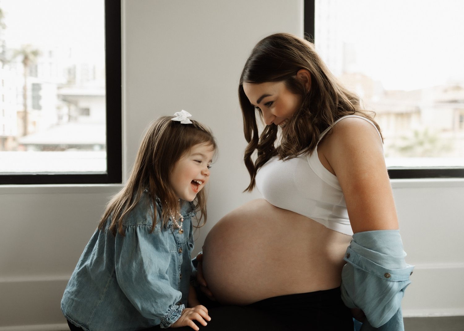 Joyful candid moment between mother and child looking at a pregnant belly.