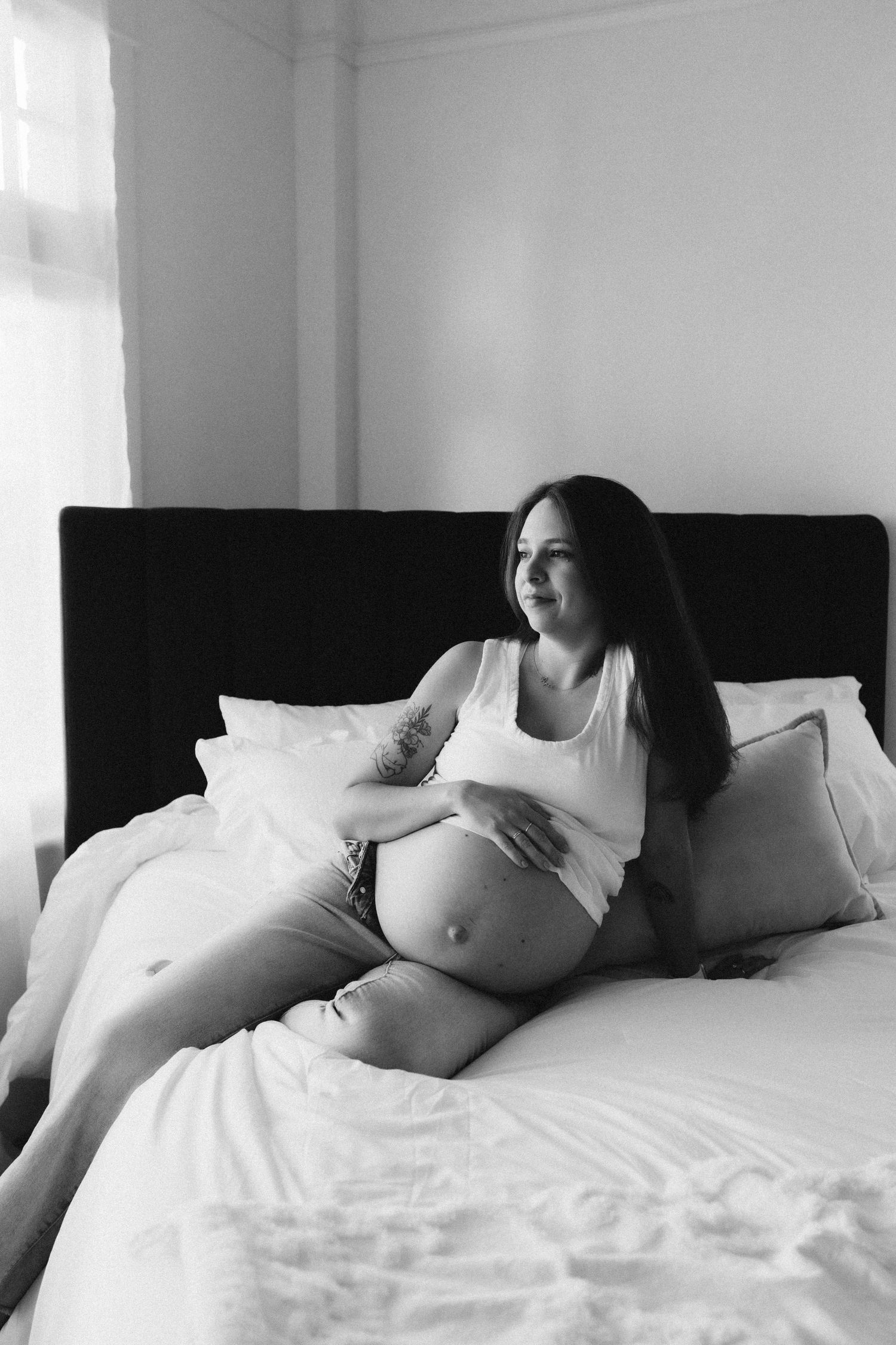 Expectant woman relaxing on black headboard bed in natural window light.
