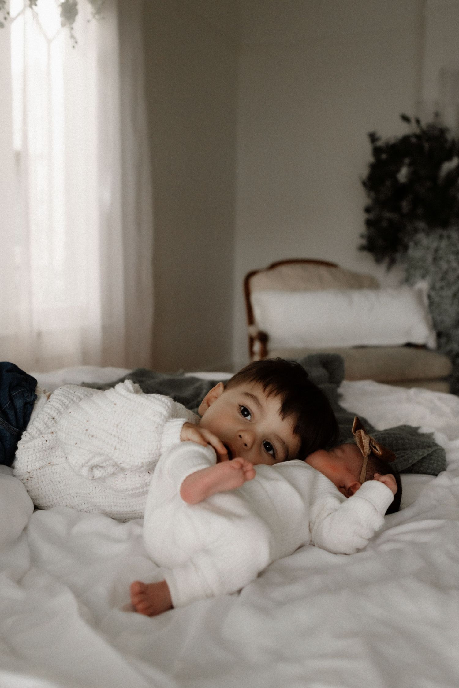 Young child in white sweater lying on white bedding in soft natural light.