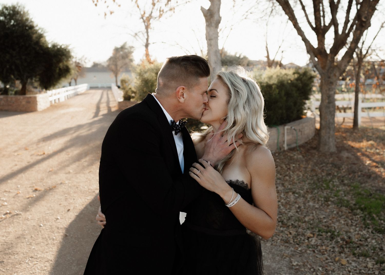 Intimate moment between a couple in formal wear sharing a kiss on a scenic path.