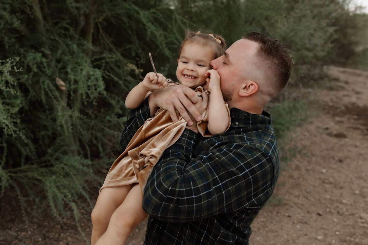 A playful moment captured between parent and child on a desert trail with green foliage in the background.