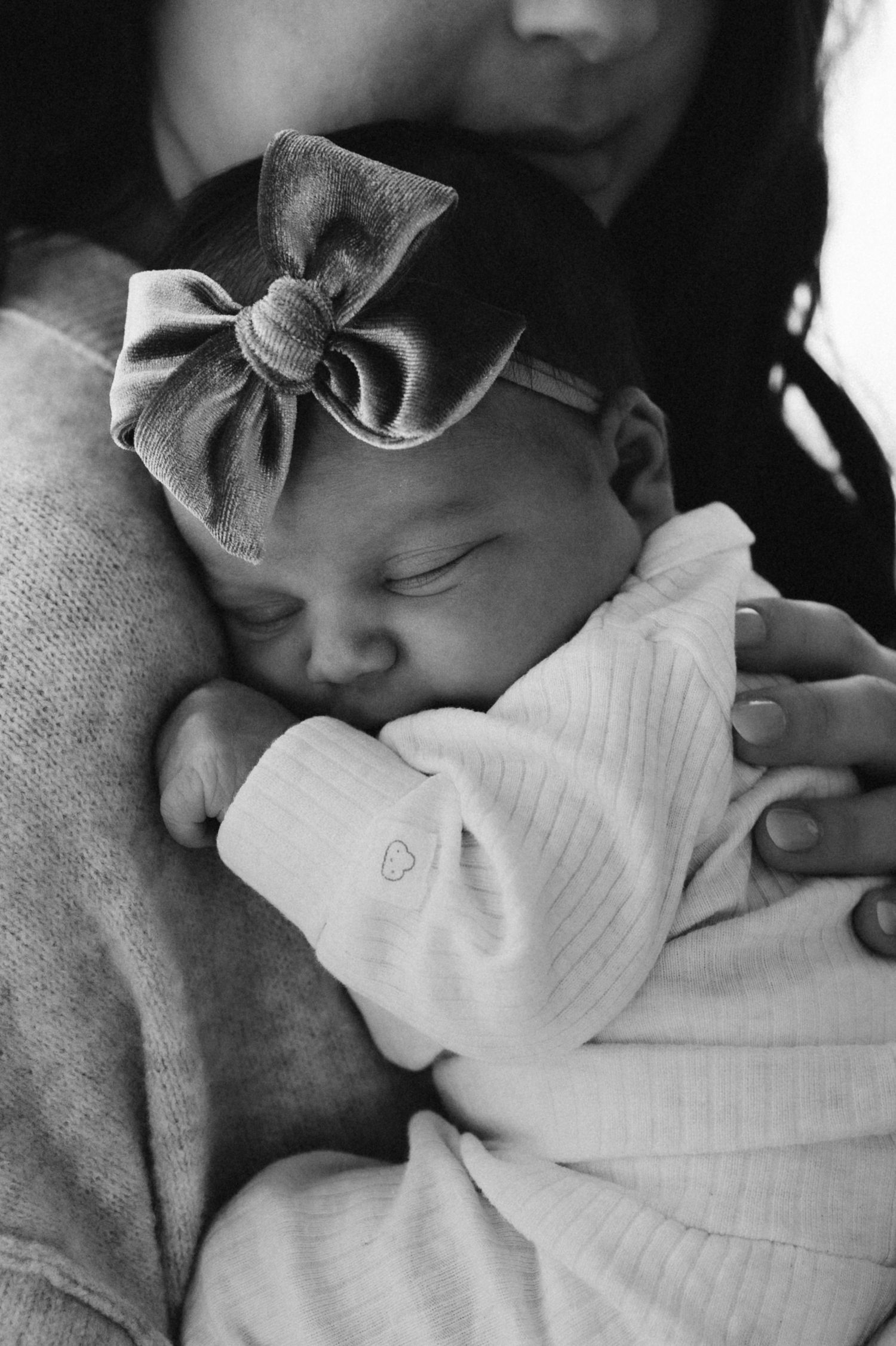 Sleeping newborn wearing bow headband rests peacefully in black and white portrait.