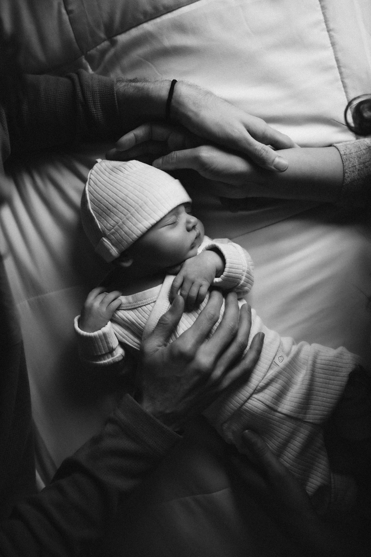 Black and white image of a sleeping newborn baby in white knit clothing being cradled.