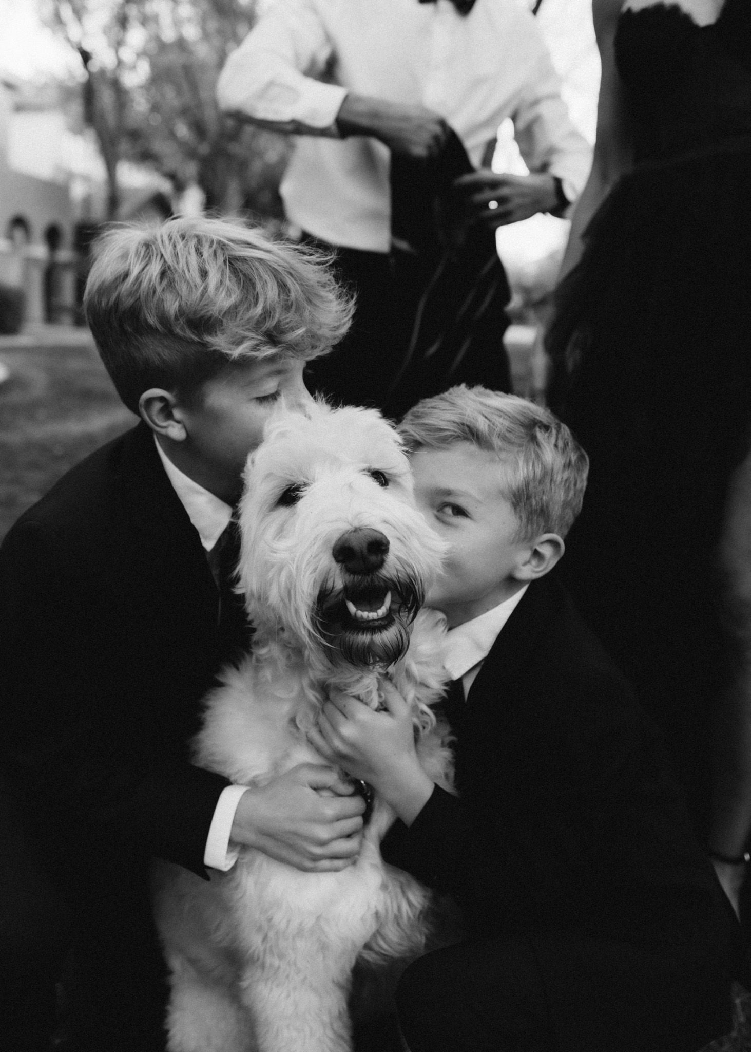 Two young boys hugging a happy fluffy white dog in a black and white photograph.