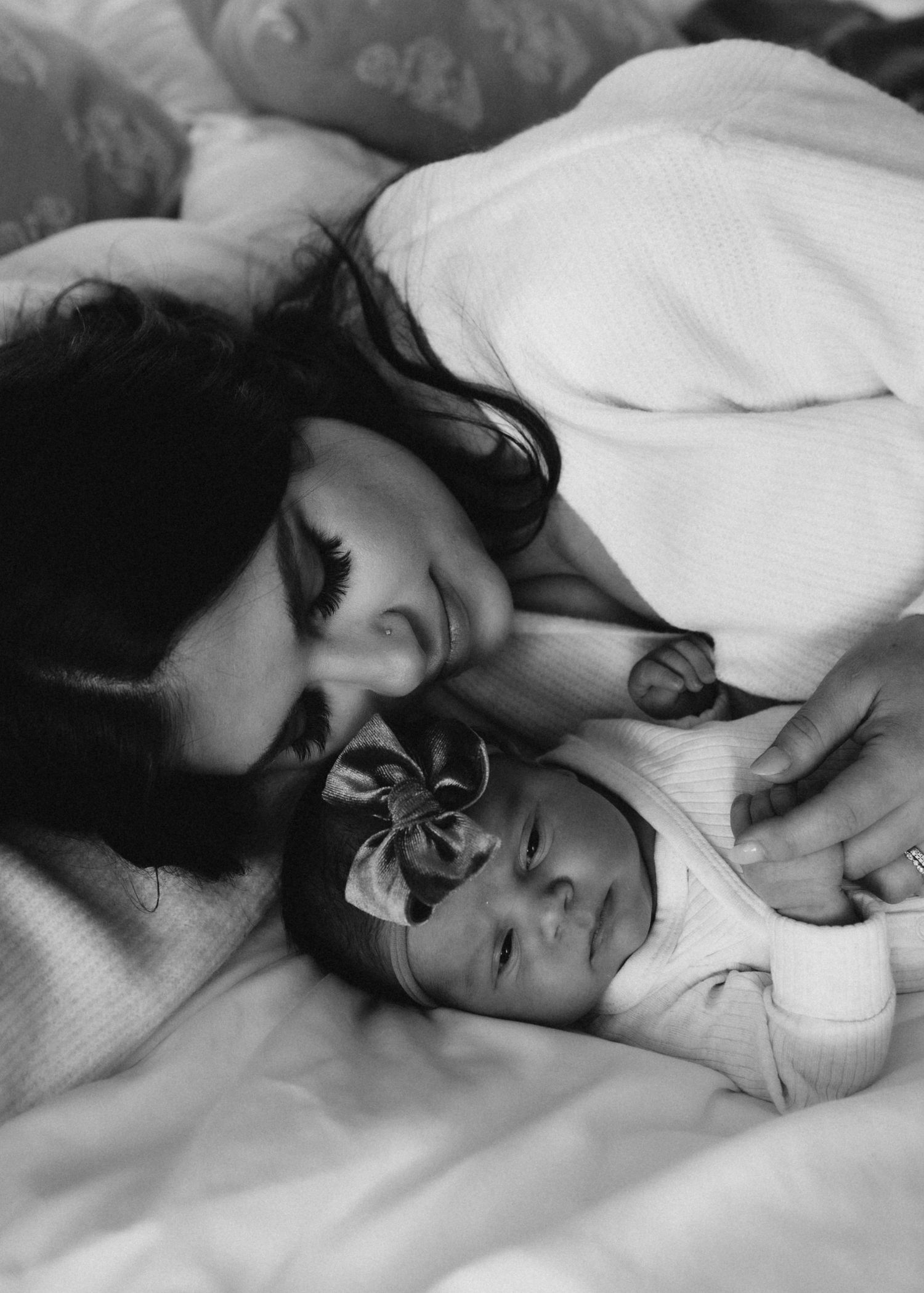 Black and white photo capturing an intimate moment between caregiver and infant on bed.