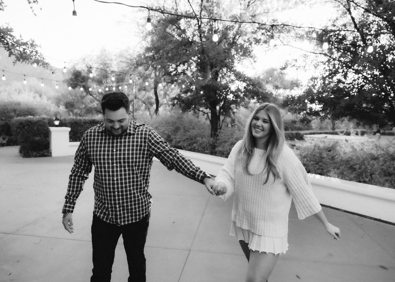 Black and white photo of a couple walking and holding hands on a paved path.