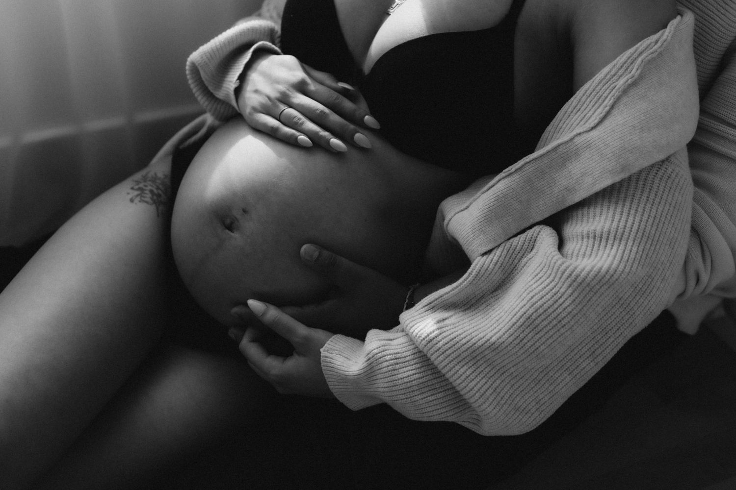 An intimate black and white close-up photograph capturing a pregnant belly in soft window light.