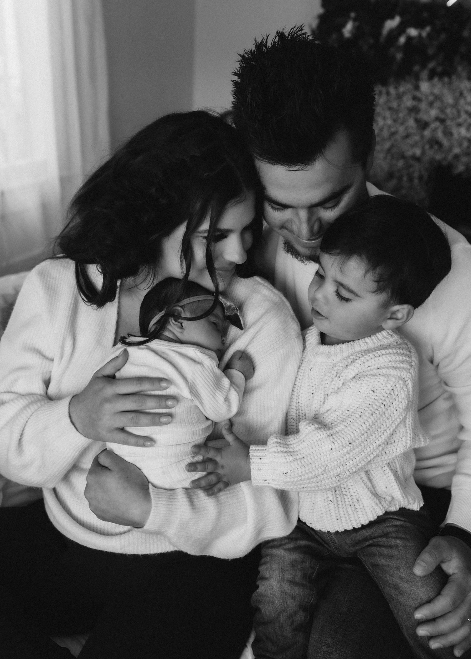 Family of four in matching white sweaters share intimate moment with newborn.