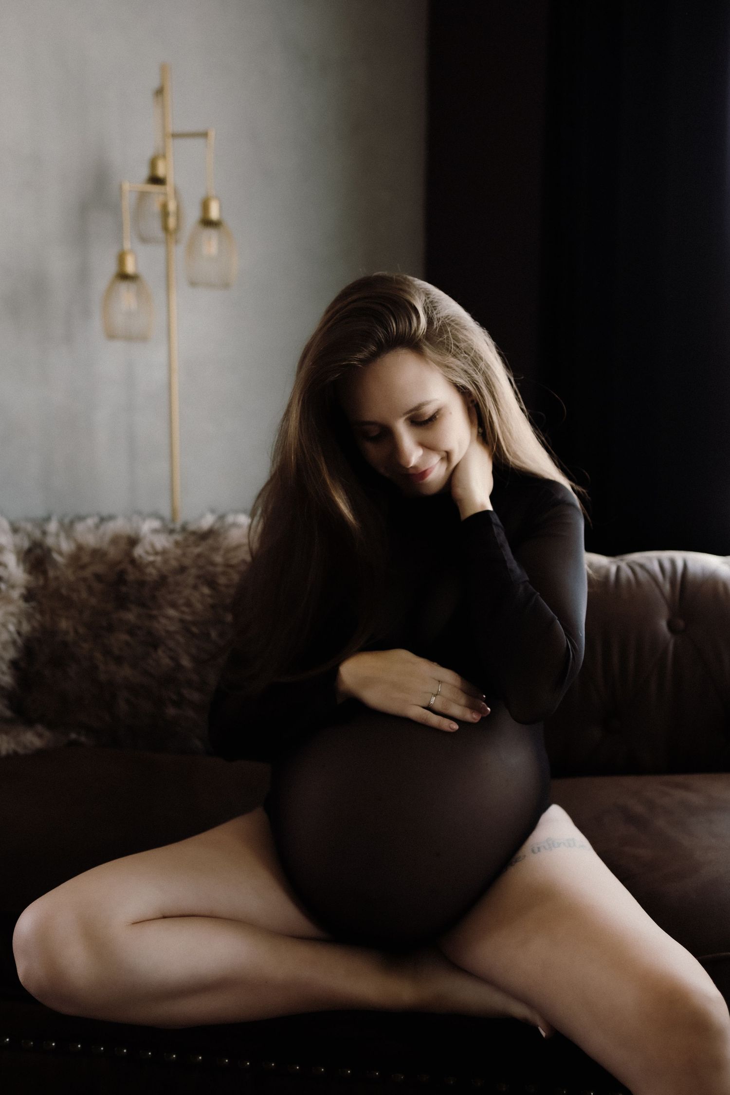 Moody maternity portrait of expectant mother in black dress on leather sofa.