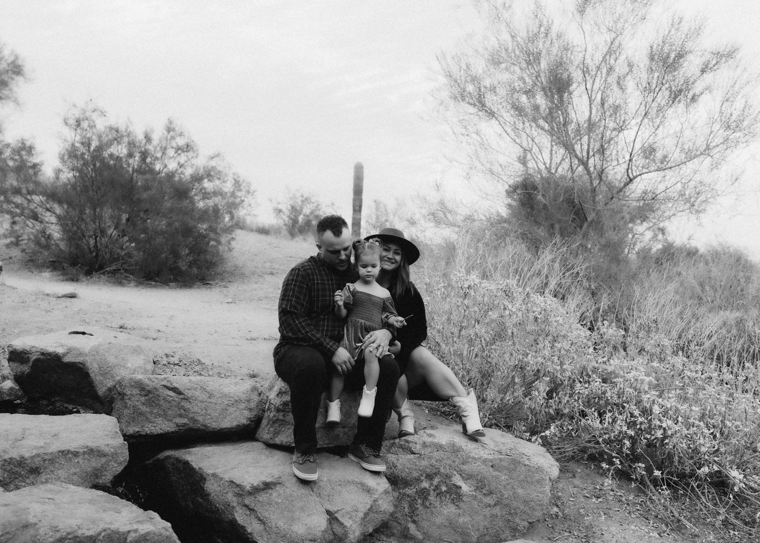 Black and white photo of a family moment on desert rocks with saguaro cactus in background.