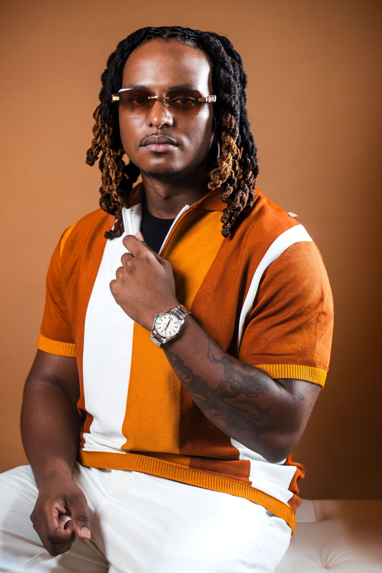A person in an orange and white sweater poses in a studio setting against a brown background.