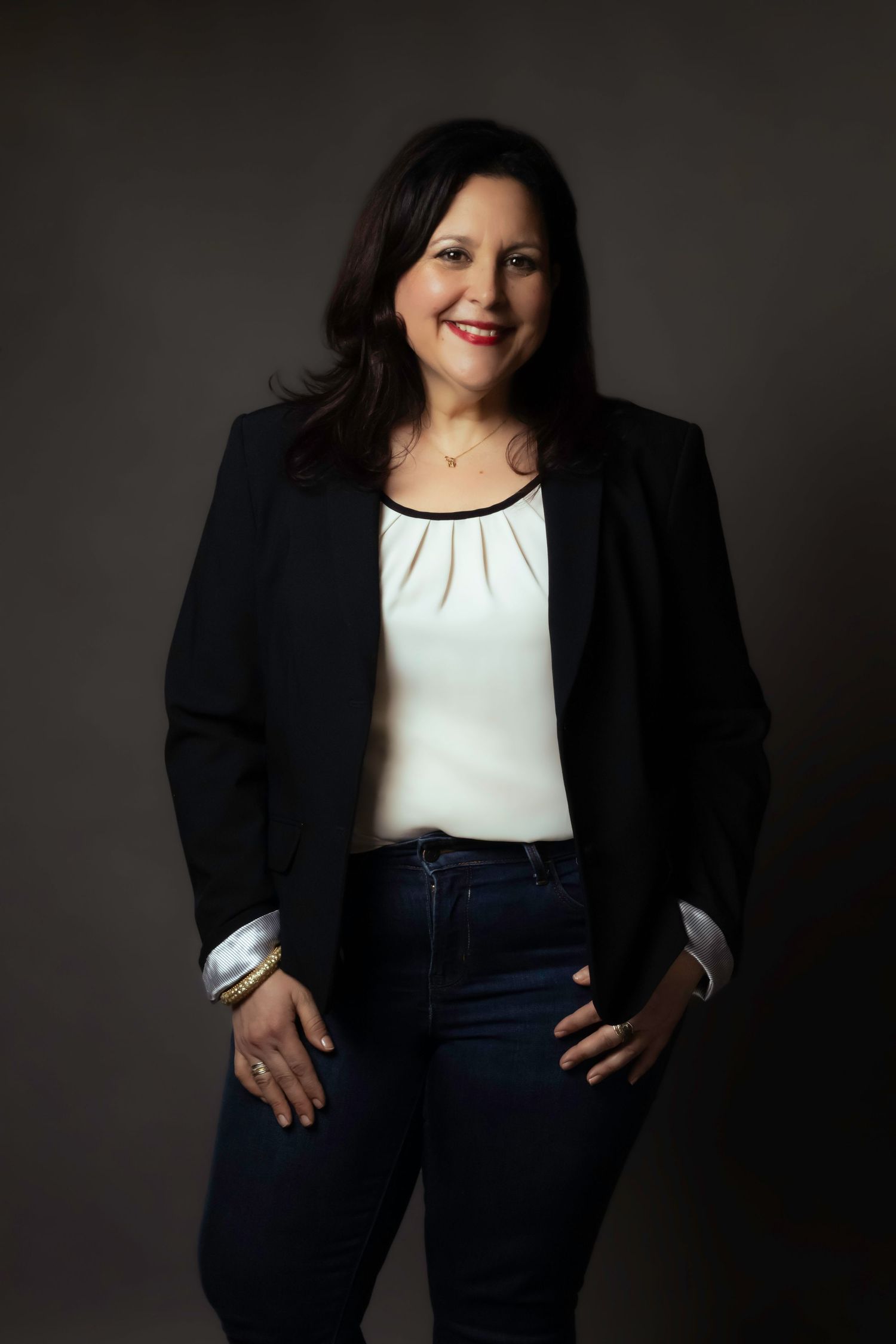Business portrait of someone wearing black blazer and white top with hands on hips.