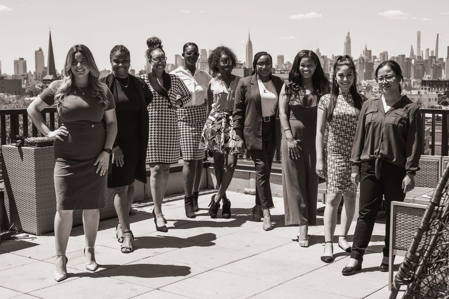 Group of women posing on a rooftop terrace with a city skyline backdrop in a black and white photo.