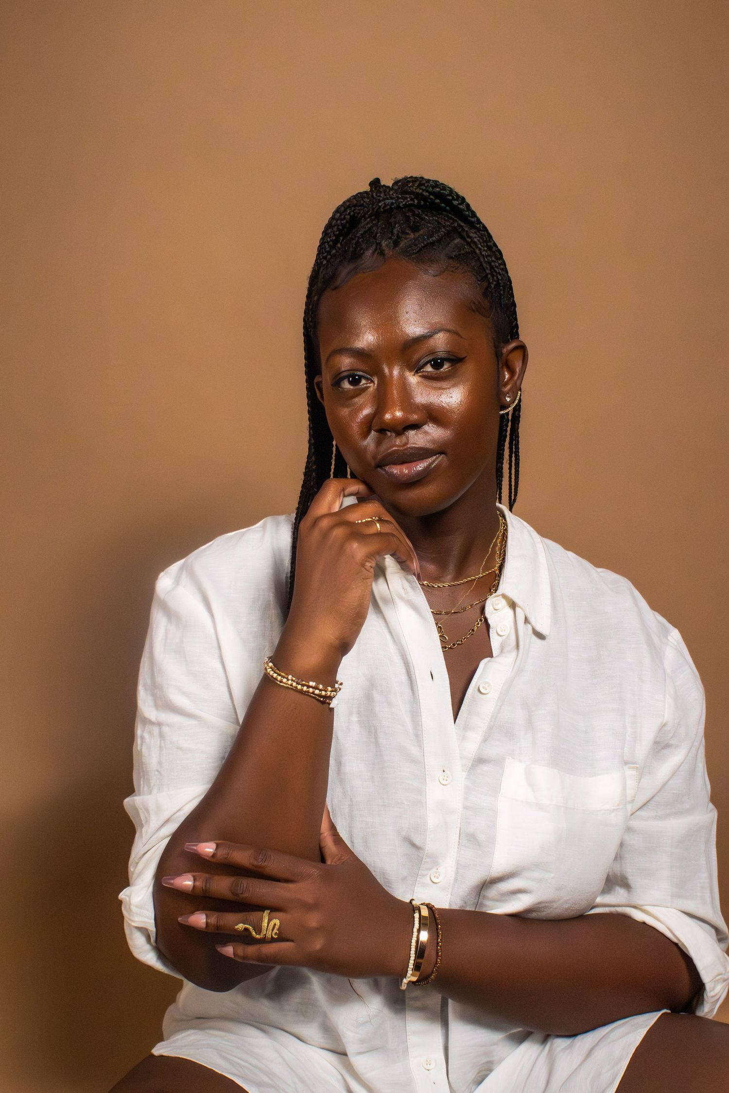 Studio portrait of a person in white shirt with jewelry against brown background.