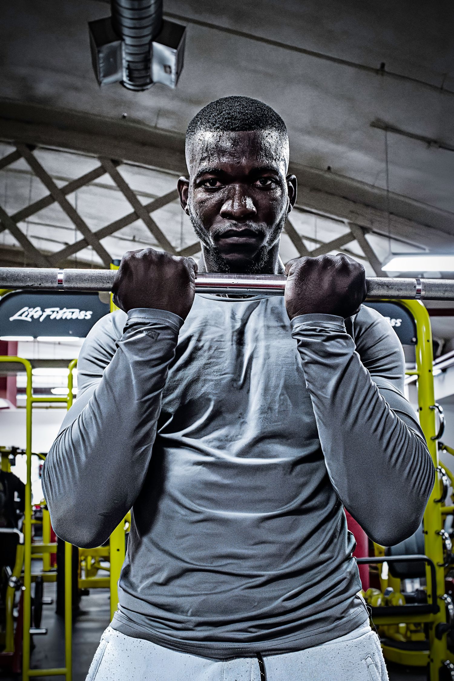 Intense workout portrait of person gripping exercise equipment in gym wearing grey athletic wear.