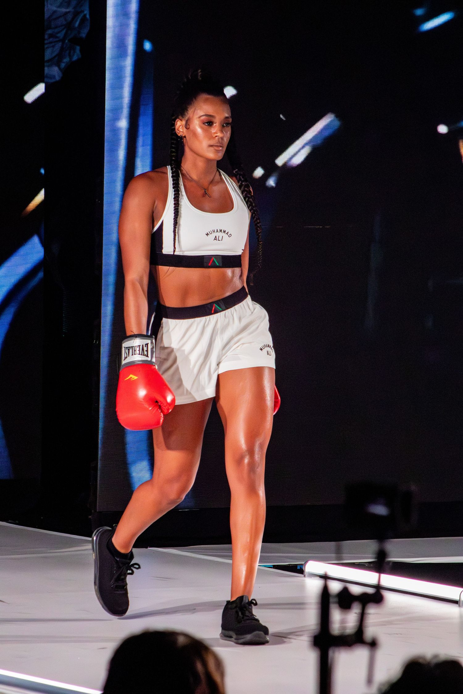 Athletic performer in white sports attire and red boxing gloves stands on stage.