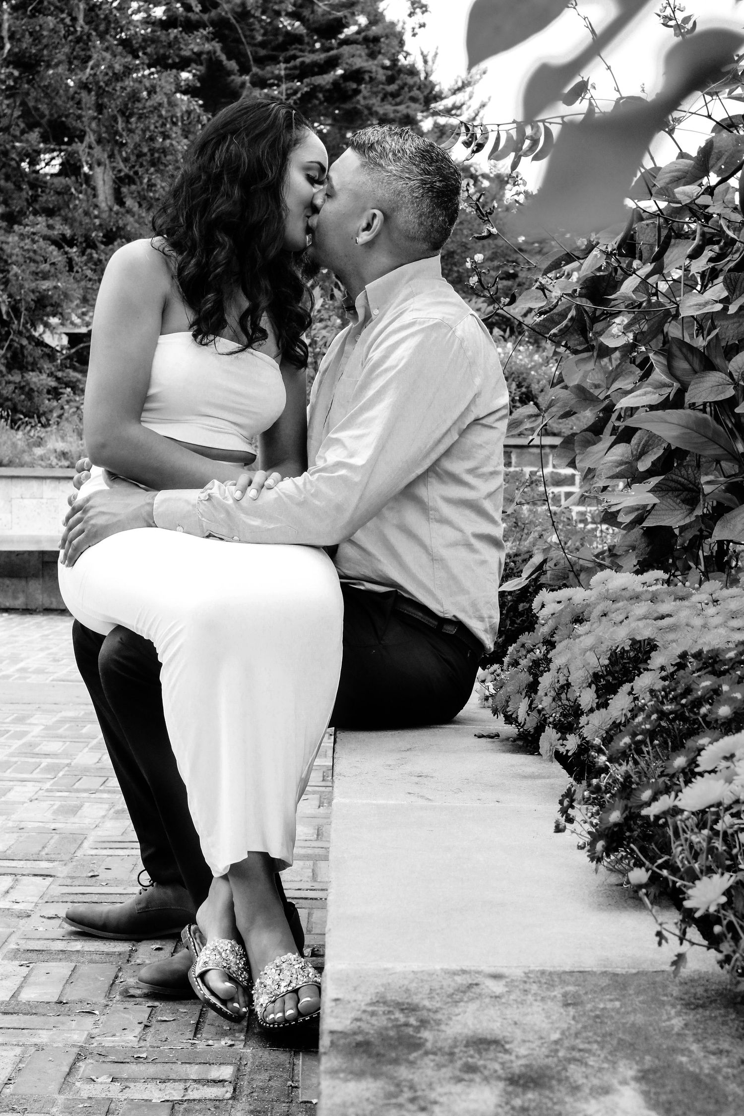 A romantic couple sharing tender moments on a garden bench in black and white photography.