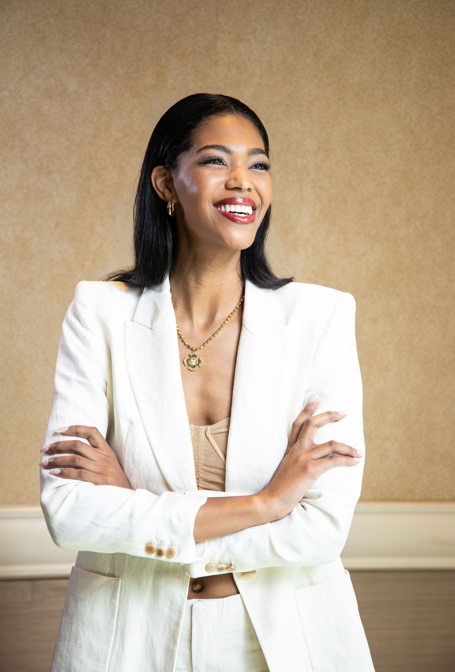 A sequence of fashion poses in a crisp white suit and gold necklace against a neutral backdrop.