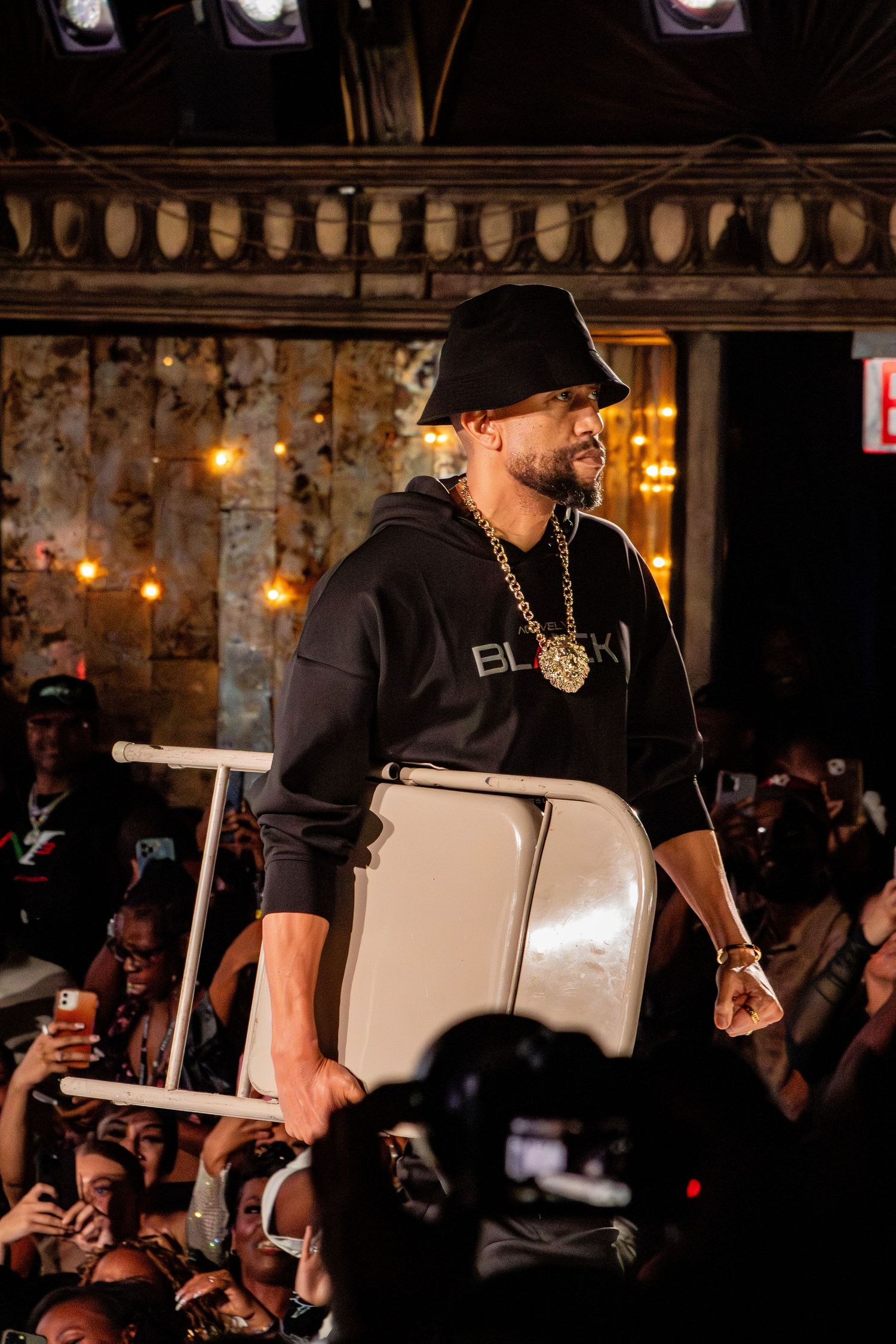 Performer in black hoodie holds white prop on stage during show.