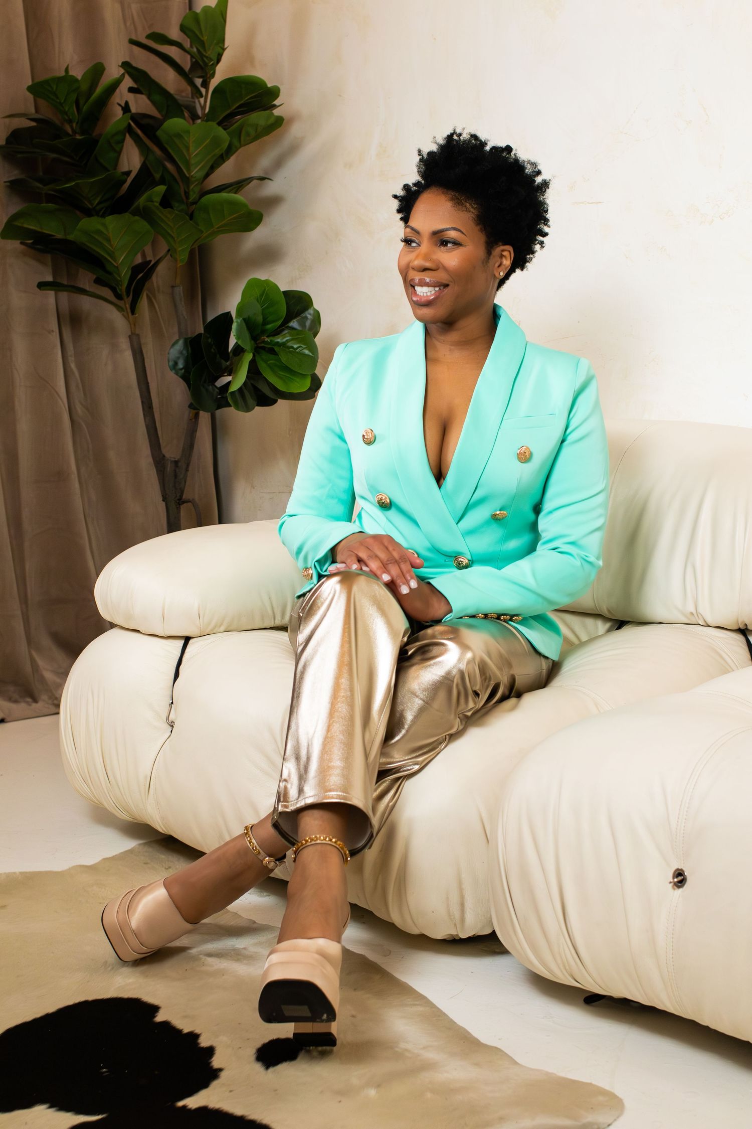Stylish portrait of person in mint blazer and metallic pants relaxing on white sofa.