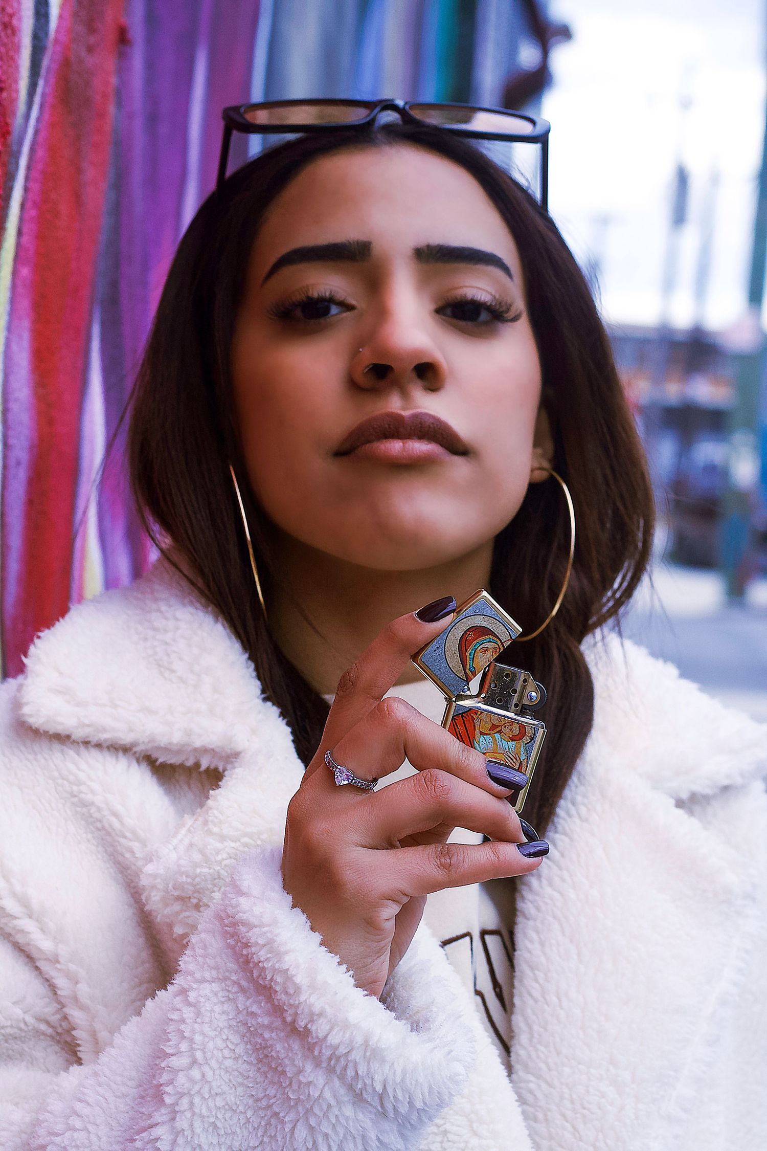 Urban style portrait in fuzzy white coat holding lighter against colorful wall.