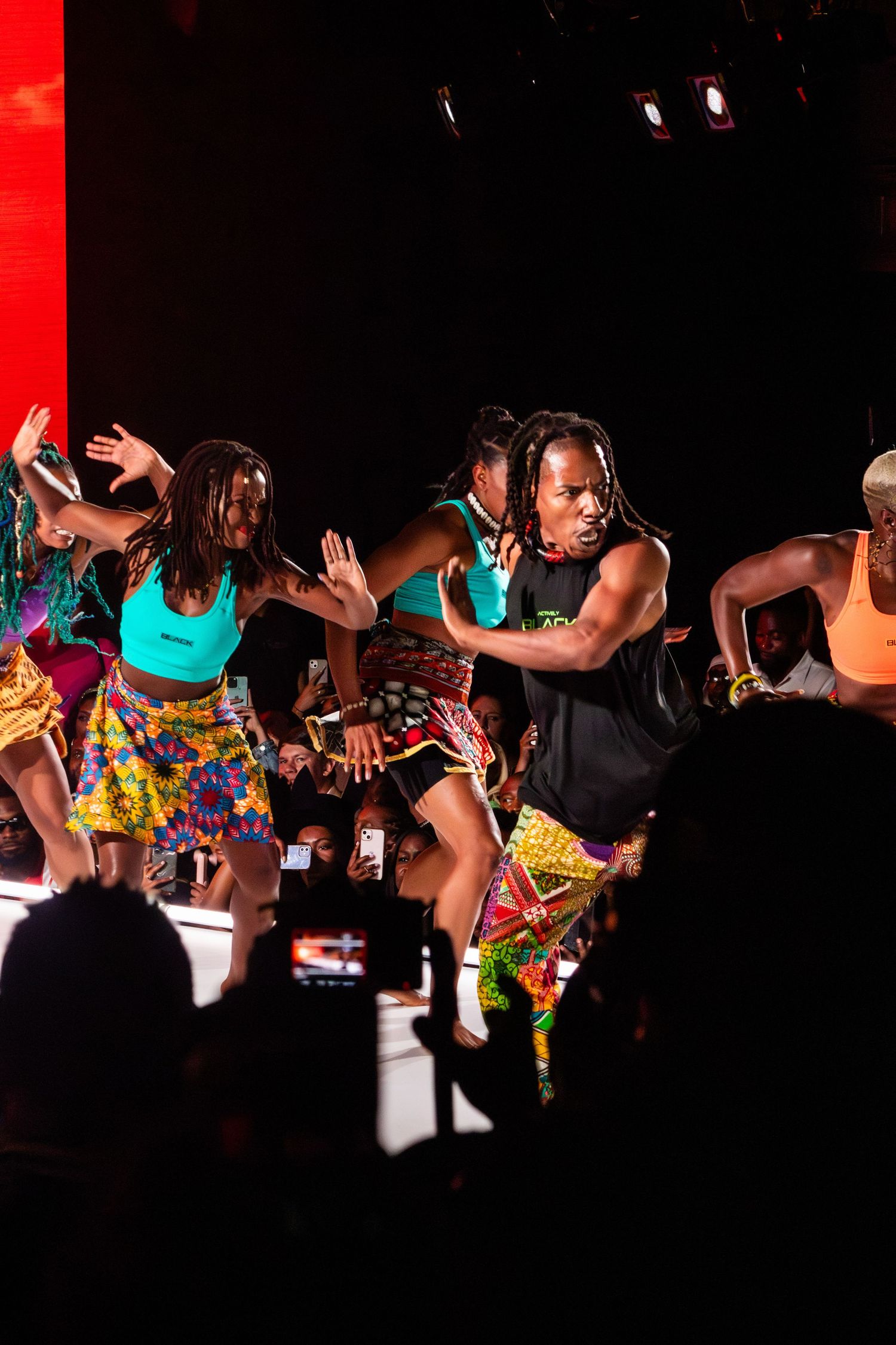 Dancers perform energetic choreography in colorful African-inspired costumes on dimly lit stage.