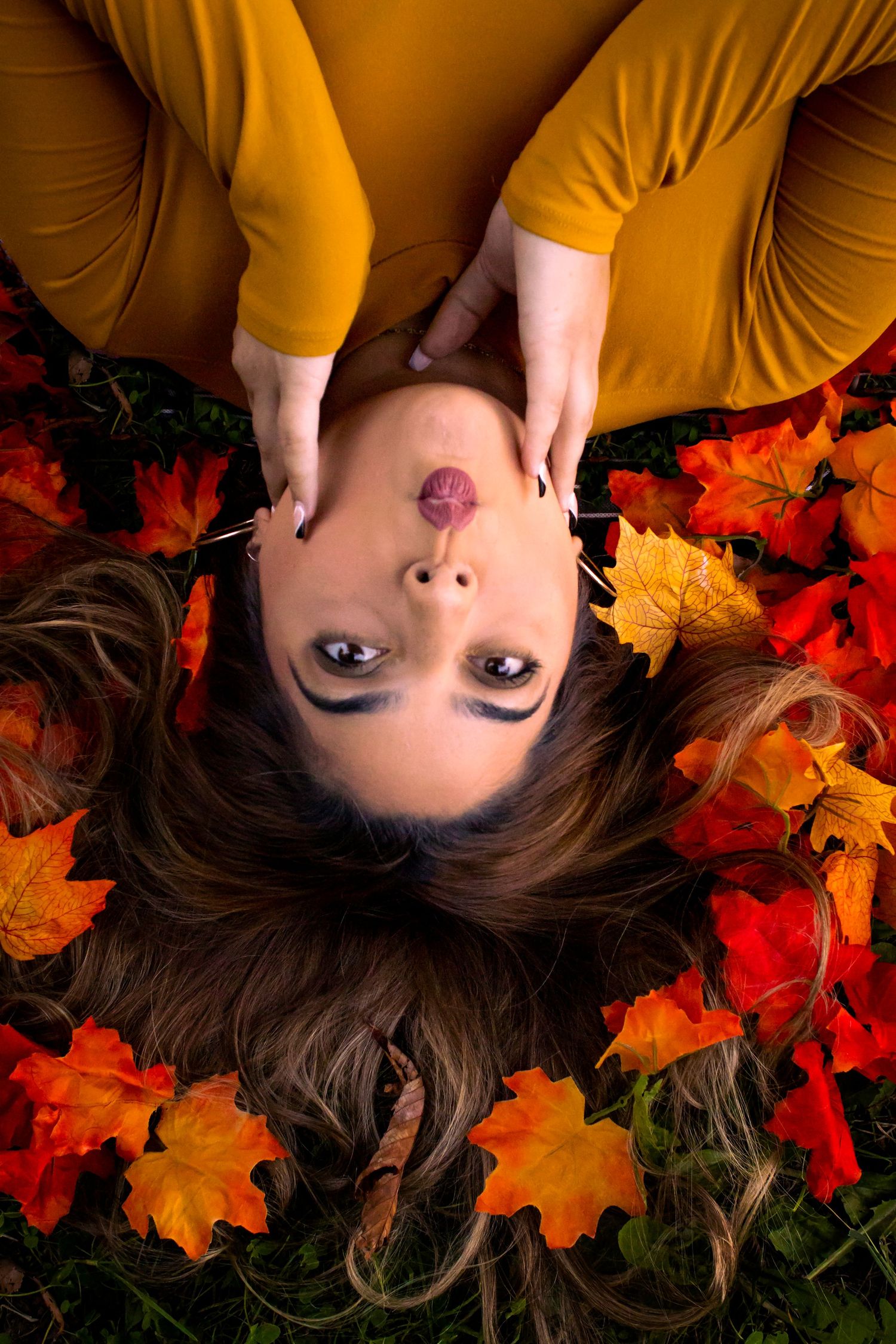 A person lies on autumn maple leaves wearing a mustard yellow top, creating a warm seasonal portrait.