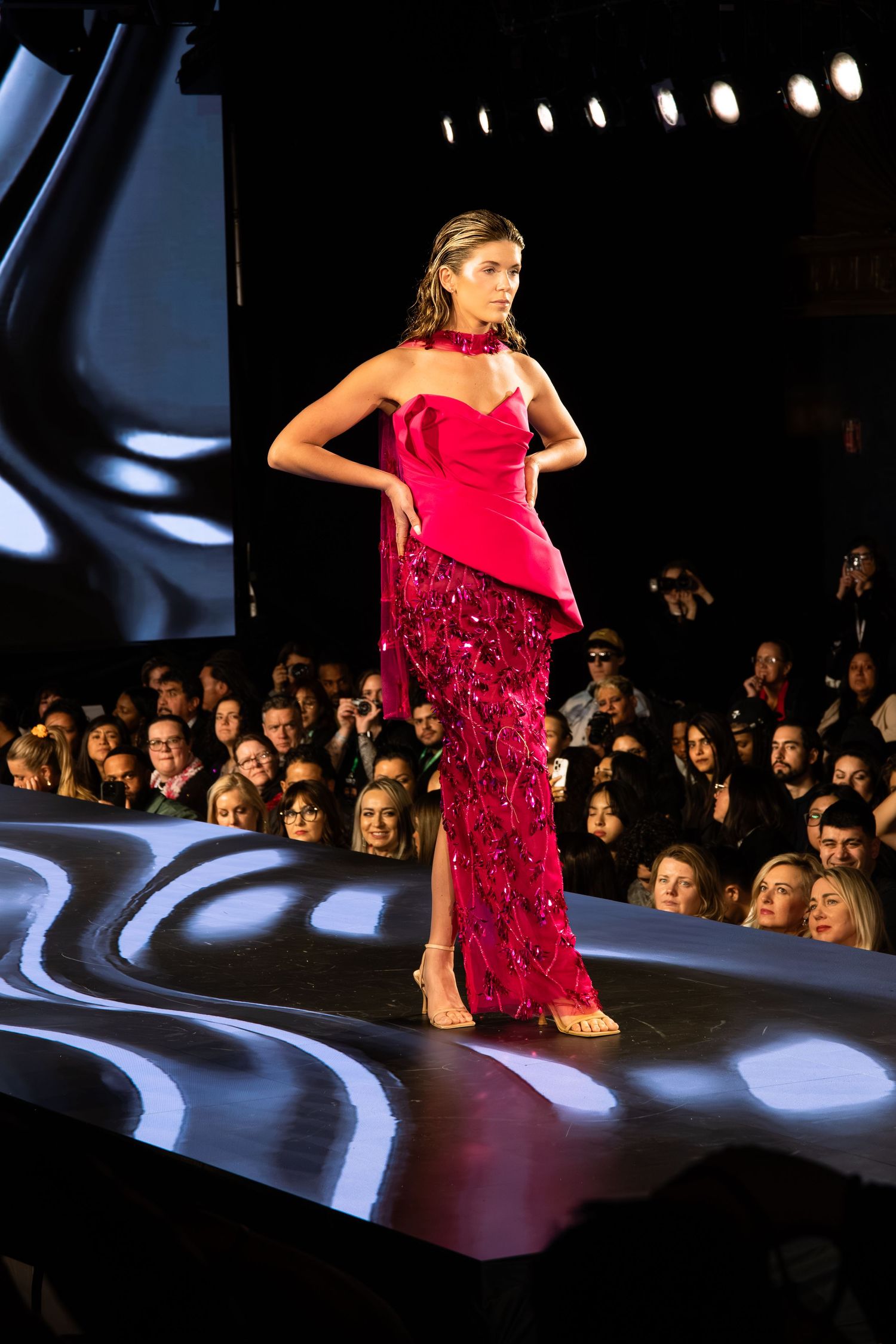 A model walks the runway in a stunning red evening gown with sequined details at a fashion show.