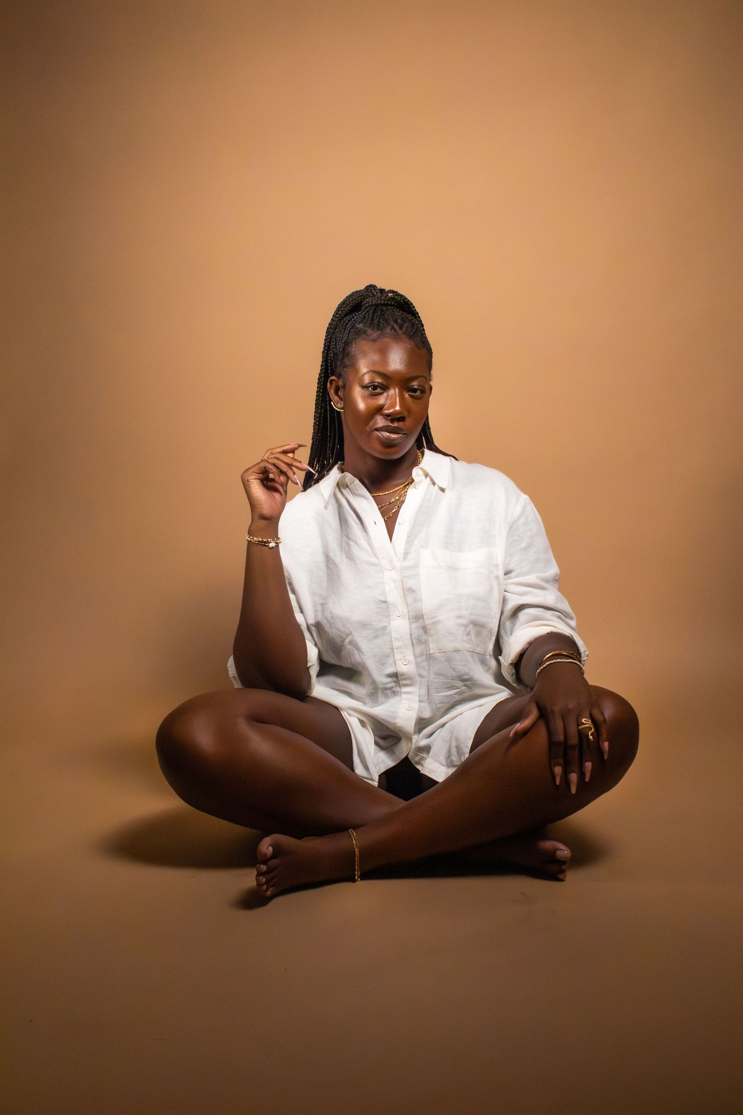 Person in white button-down shirt sits cross-legged against brown studio backdrop.