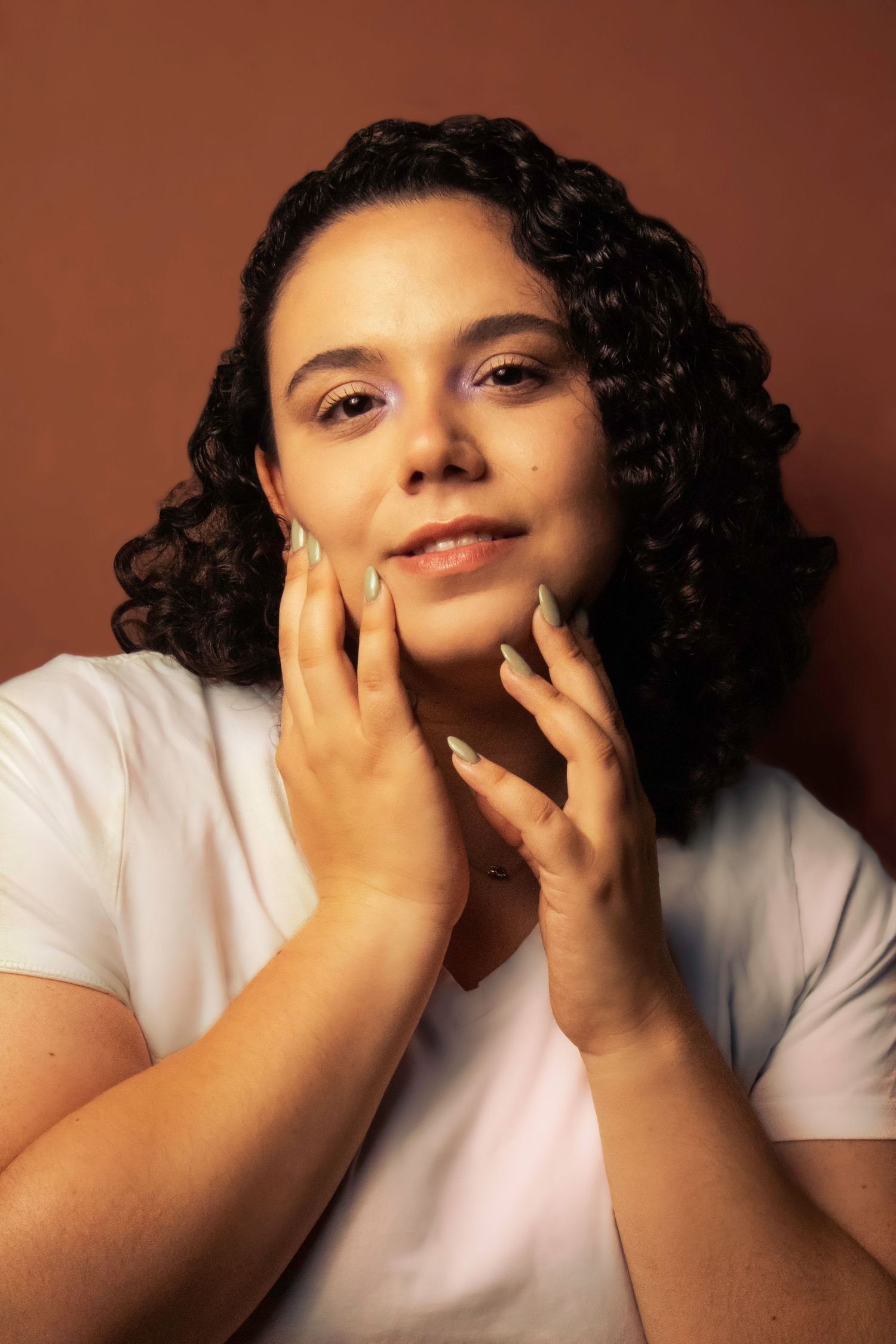 Natural beauty portrait with curly hair in white t-shirt against brown background.