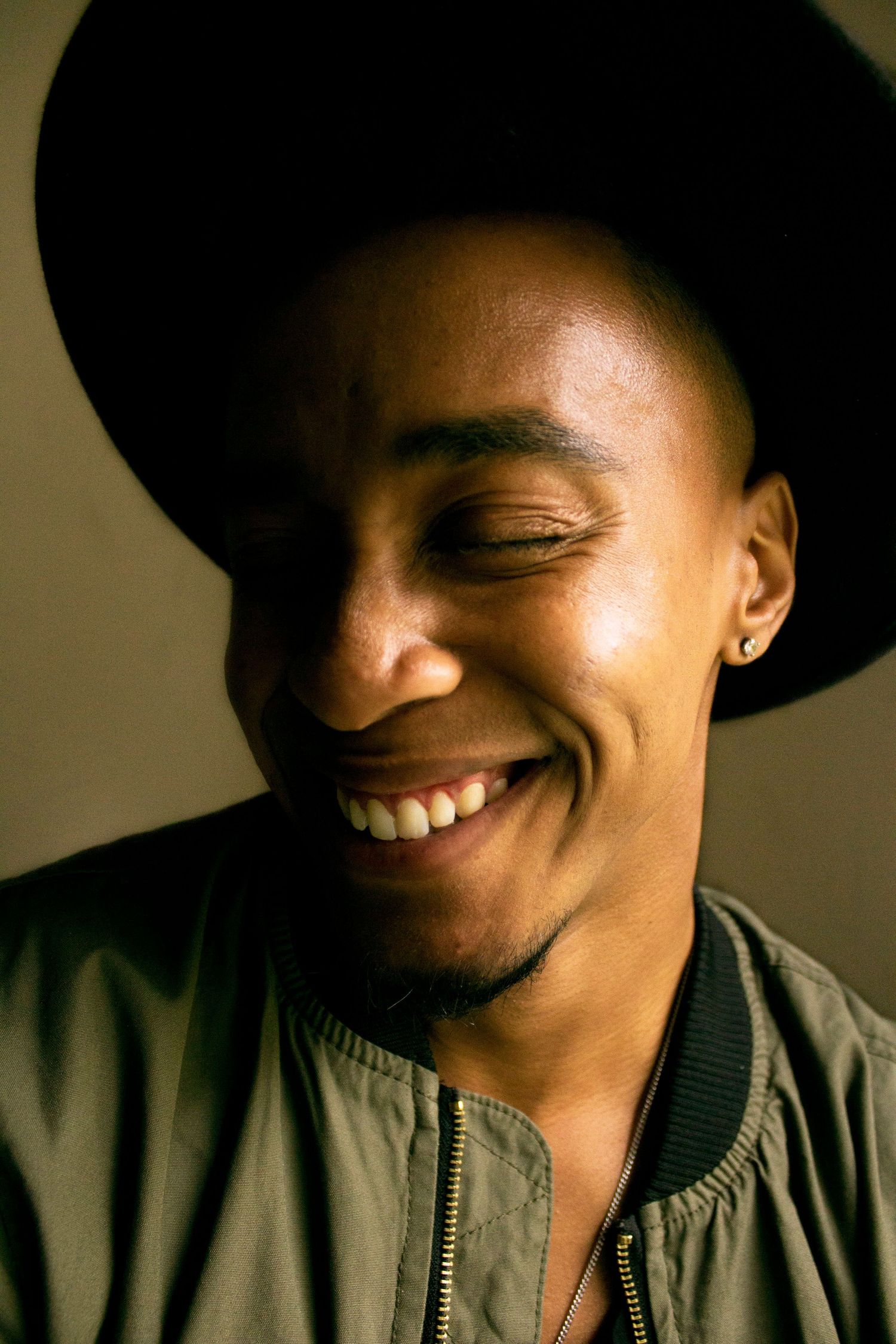 Candid joyful moment captured in dramatic lighting wearing a black hat and bomber jacket.