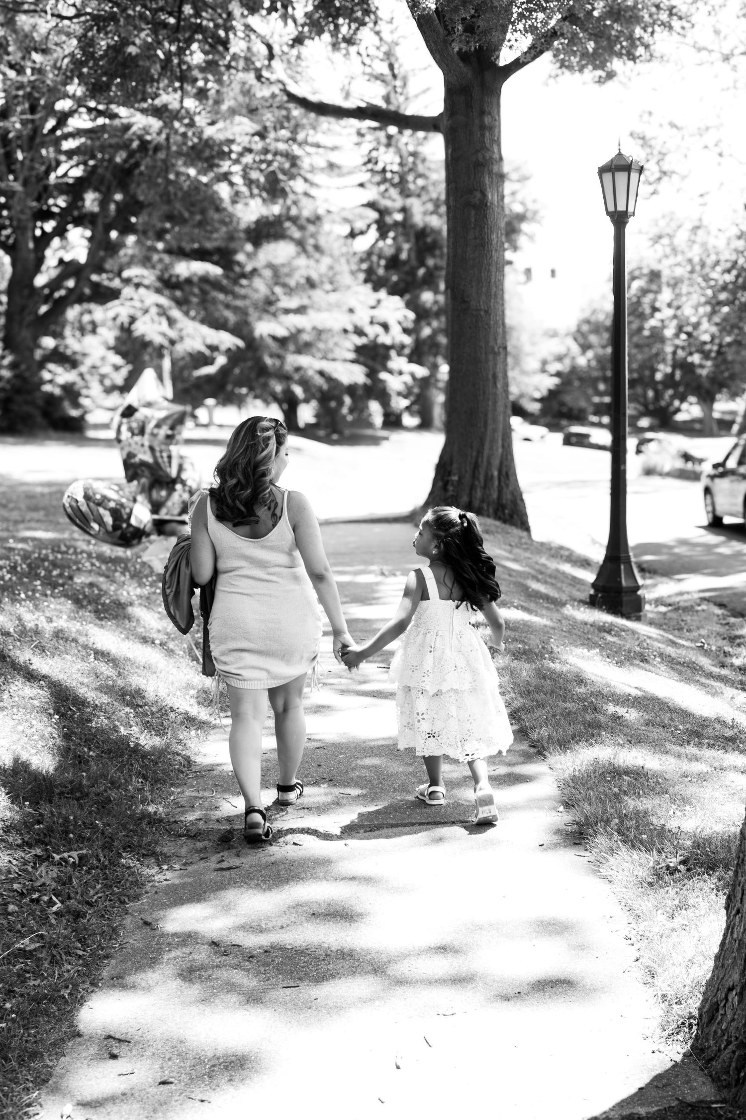 Black and white photo of parent and child walking hand in hand on a tree-lined path.