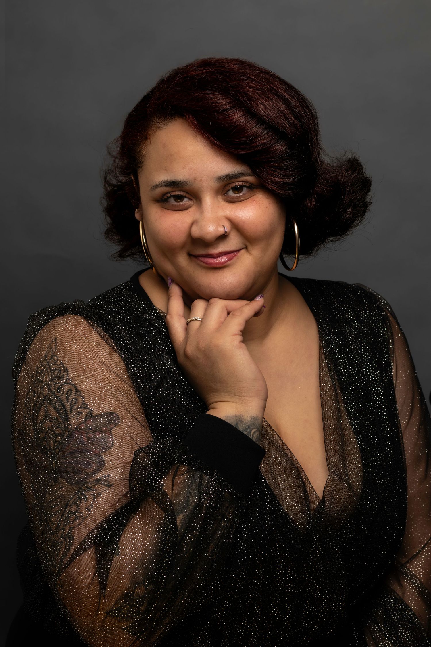 Elegant portrait in black sheer sleeve dress showing tattoo art and warm expression.