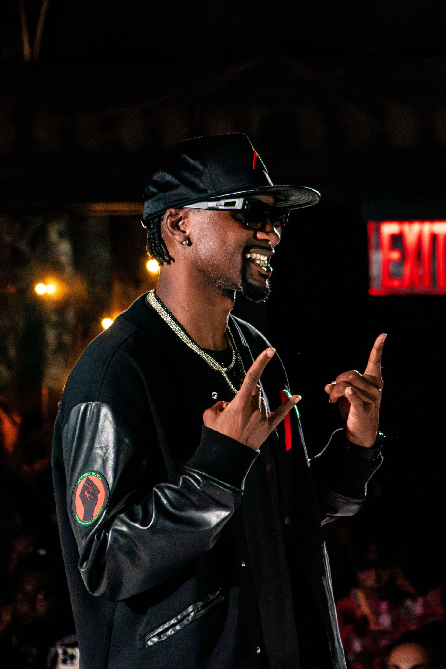 Performer in dark jacket and baseball cap gestures with hands during nighttime show.