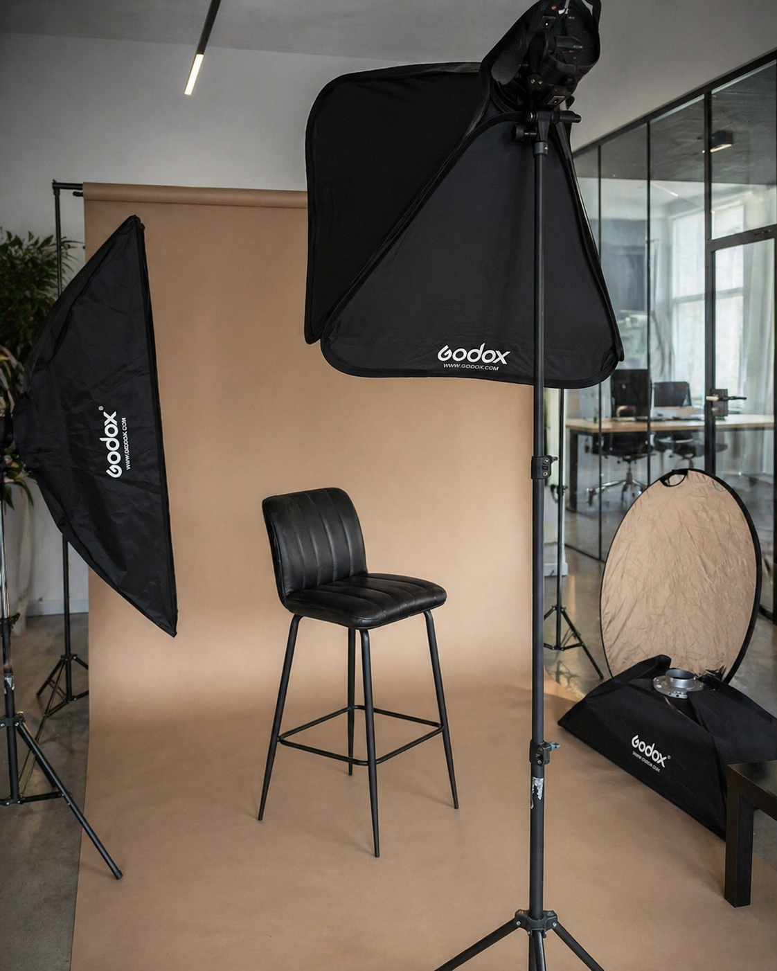 Professional photo studio setup with Godox softbox lights, a black bar stool, and beige backdrop for portrait photography.