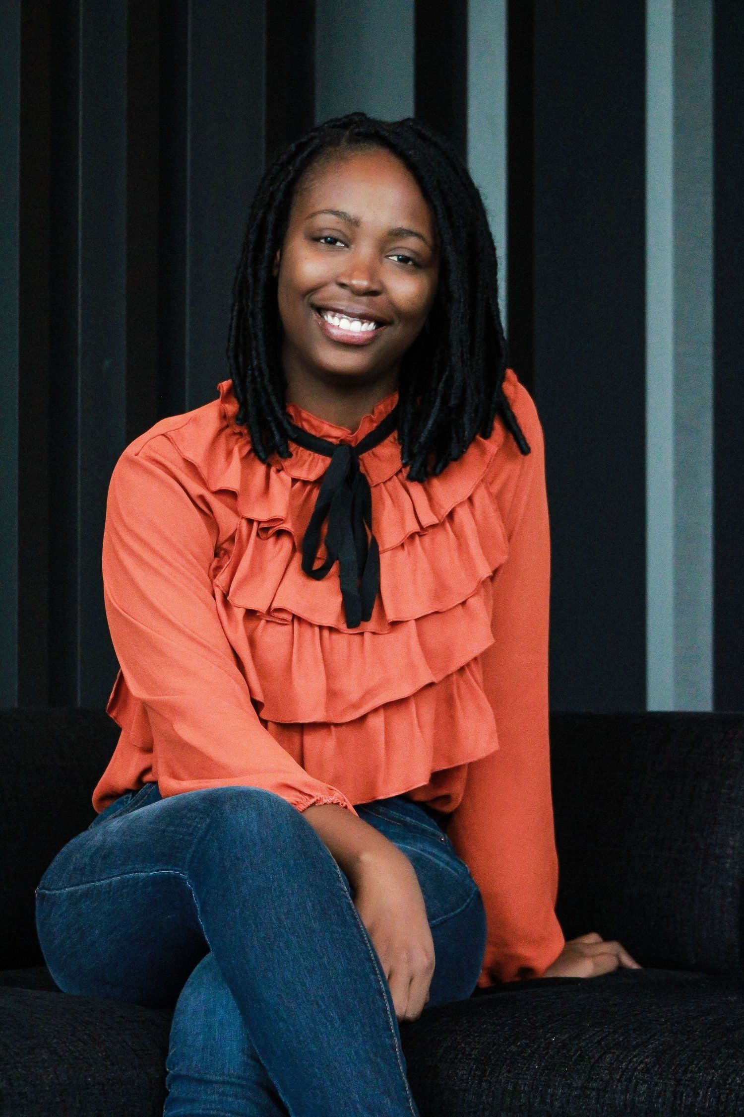 Casual indoor portrait showcasing a coral ruffled blouse paired with denim on a dark couch.