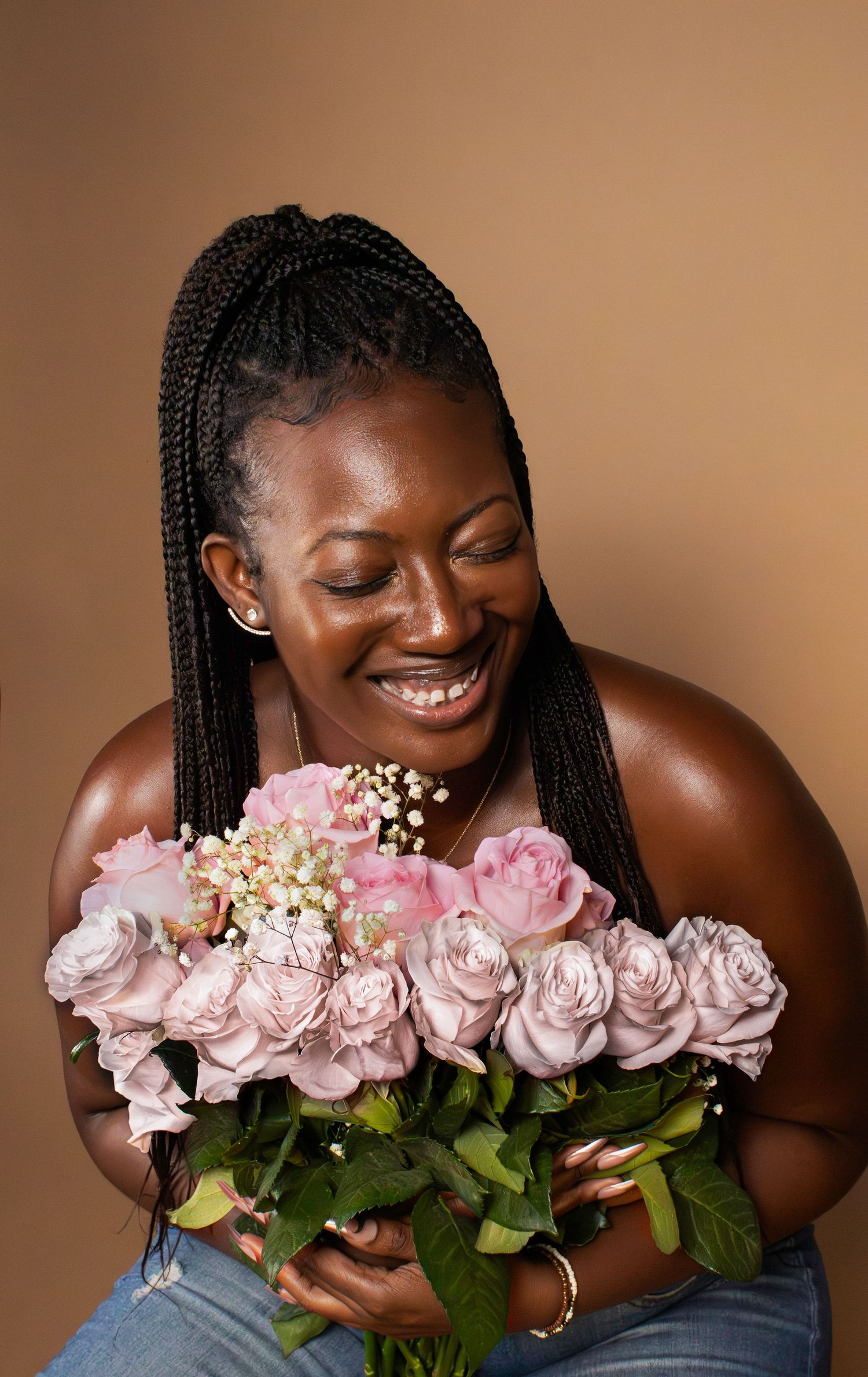 A joyful portrait with pink roses and braided hair against a warm brown background.