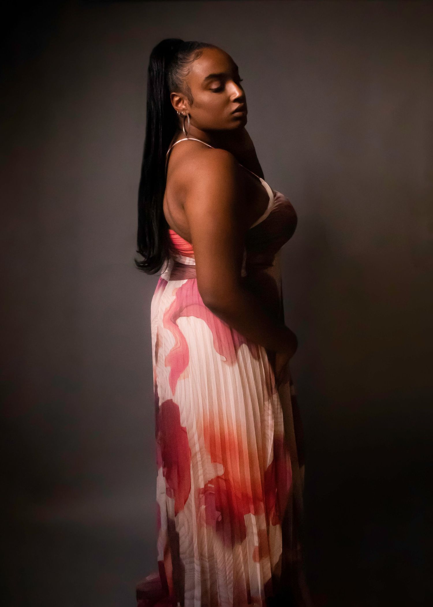 Elegant side profile portrait of someone in a flowy pink and white floral dress against dark background.