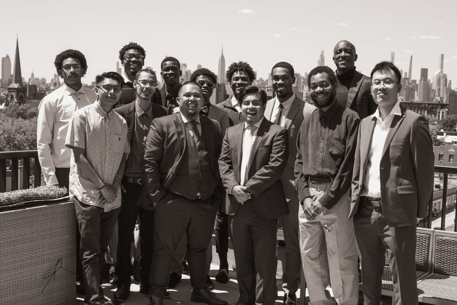 Group of young men posing together on a rooftop with New York City skyline in the background, black and white photo.