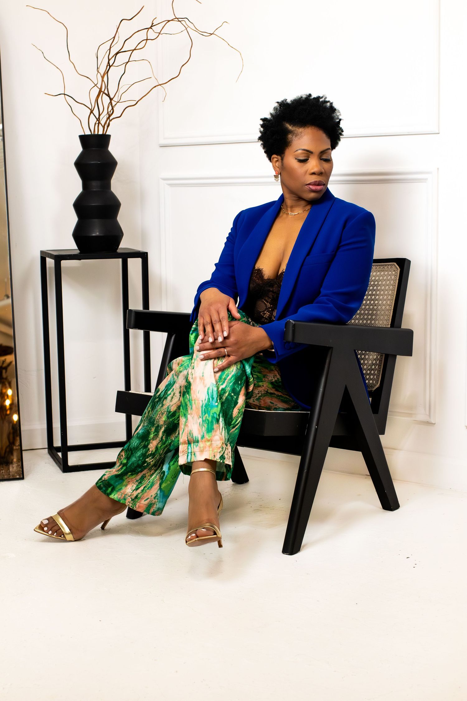 Elegant studio portrait with person in blue blazer seated by decorative black vase and branches.