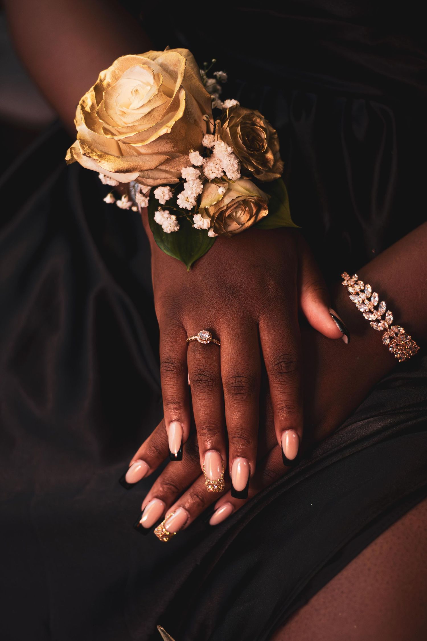 Close-up of hands wearing elegant ring and corsage with golden roses.