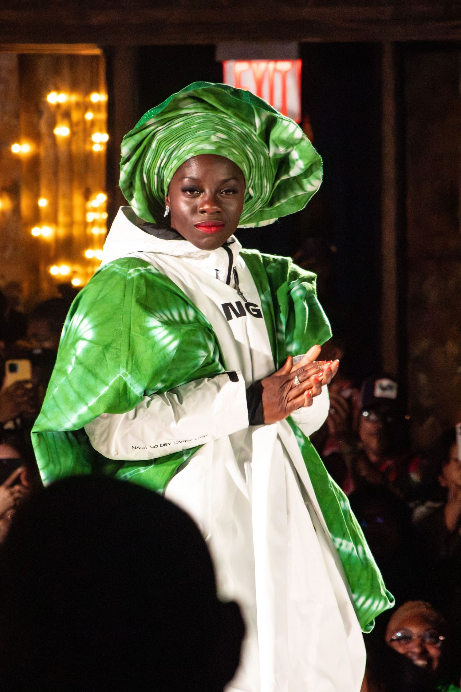 Model showcases dramatic white and green satin ensemble with matching head wrap on runway.