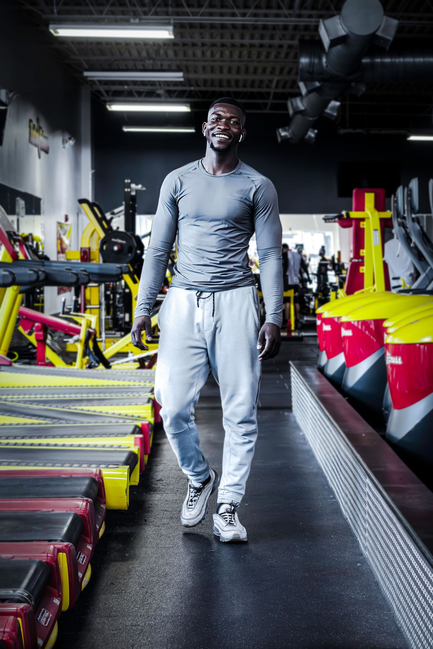 Athletic figure in grey workout clothes standing confidently in modern gym with equipment.