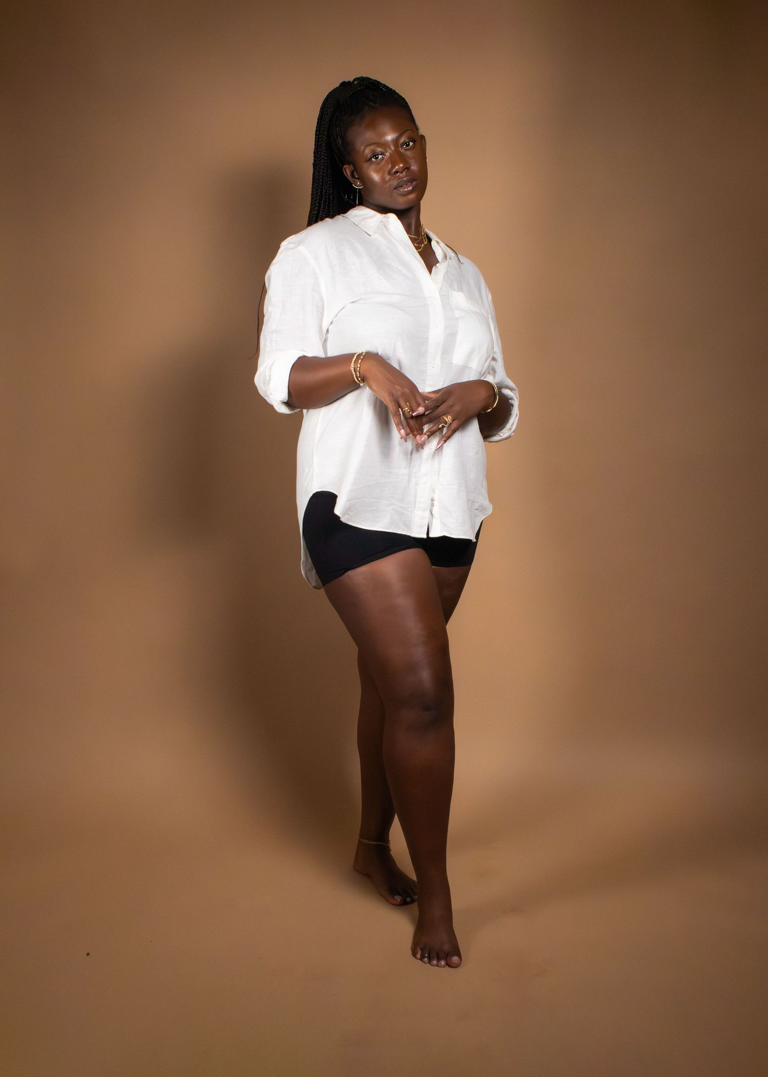 Person poses in white shirt and black shorts against warm brown studio background.