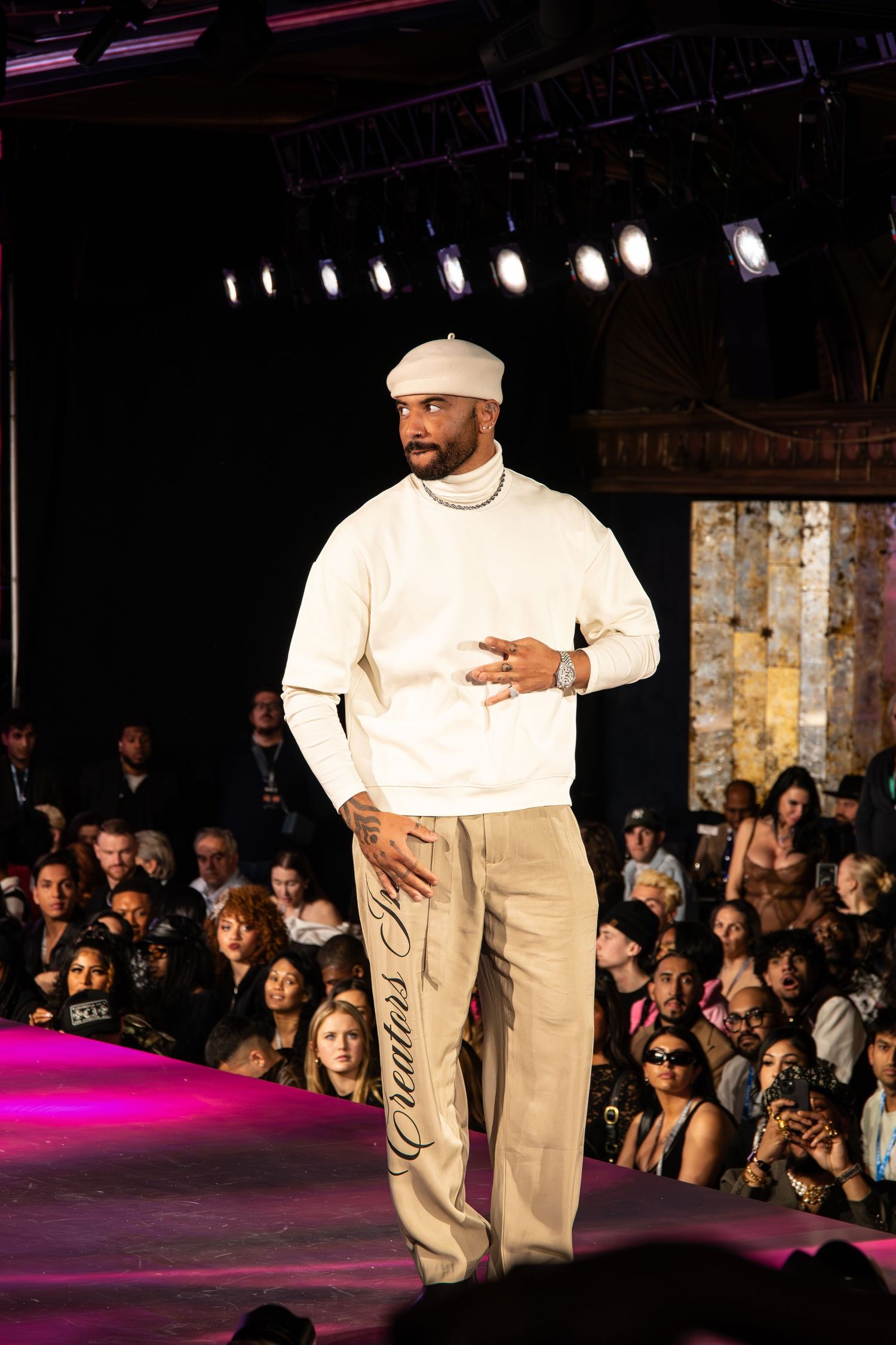A model walks the runway wearing a white turtleneck sweater, cream beret and khaki pants during a fashion show.