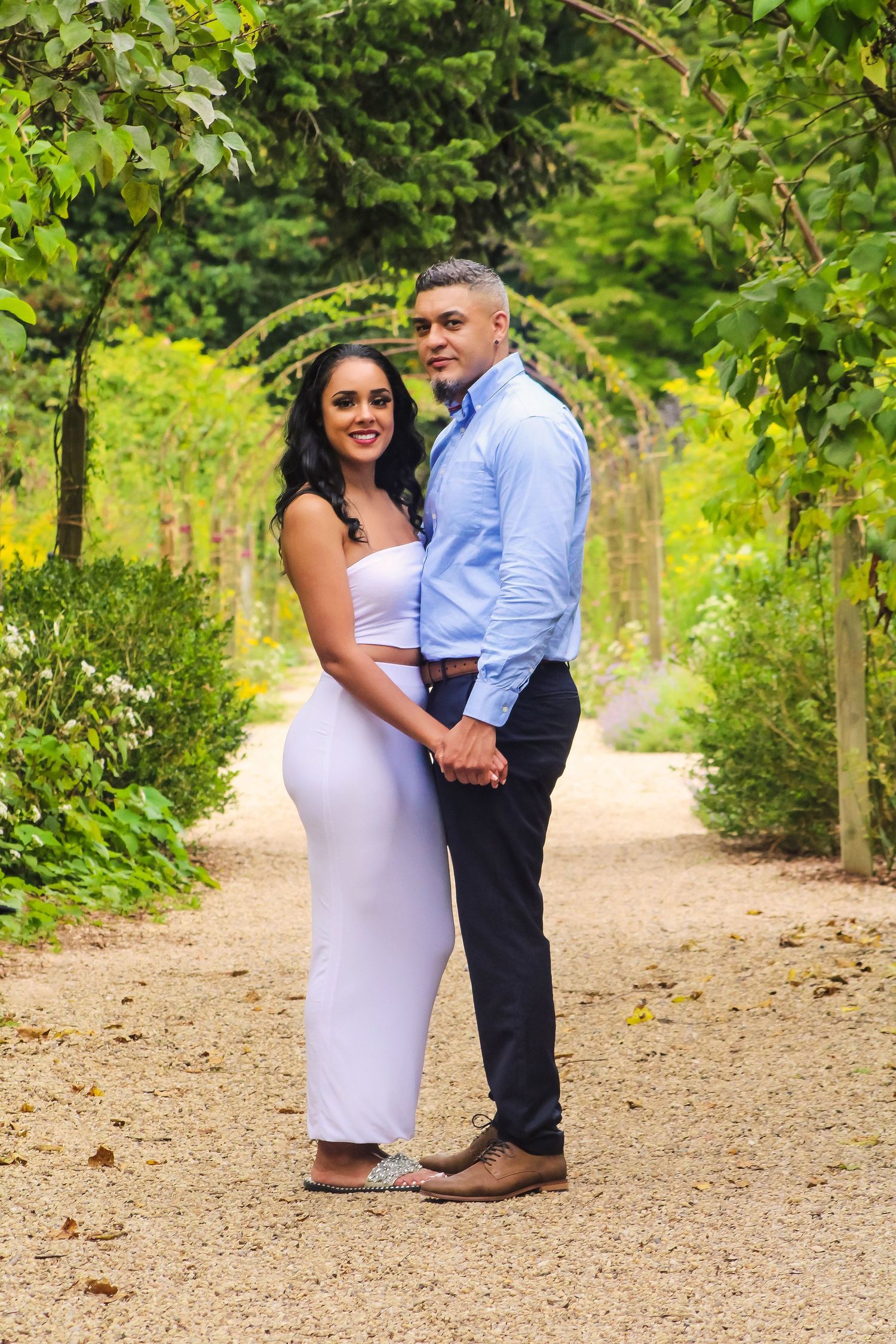A couple shares romantic moments along a tree-lined path in a natural outdoor setting.