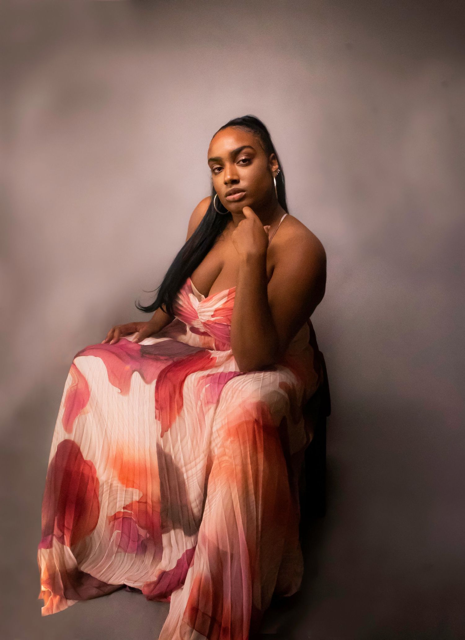 Graceful portrait of someone wearing a flowing pink and white pleated dress in dramatic lighting.
